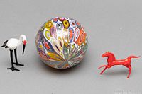 Photo showing the three items in the lot: the round colorful Millefiori glass ornament, the stork figurine, and the red horse figurine. Displayed on grey background.