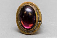 Close-up front view of the oval purple Murano glass cabochon set in a brass ring base, showing the glass's deep color and surface reflections.
