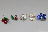 Four pairs of vintage Italian glass grape cluster earrings arranged together on a neutral surface. Visible are the red cherry clusters with green leaves, clear grape cluster earrings, and cobalt blue grape cluster earrings
