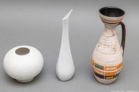 Front view of two white textured bud vases and one colorful hand painted pitcher.