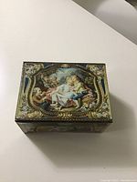 Top view of the biscuit tin showing detailed classical painting on lid with ornate border.