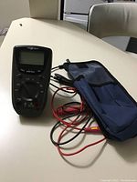 Full view of Nexx Tech battery tester atop a white table, showing unit, test leads, and blue carrying case.