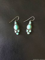 Front view of the pair of turquoise drop earrings on black background