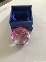 Pink faceted crystal pyramid resembling a diamond, sitting in front of a blue Birks box with satin interior padding.
