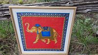 Framed scarf with a red background featuring a gold elephant with blue adornments and a blue and gold floral border, set in a cream frame with gold trim.