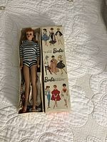 Barbie doll inside original box with illustrated lid showing vintage fashion models.