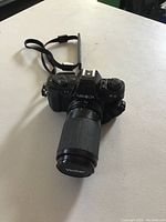 Front and side view of Minolta X-9 camera with Vivitar lens and strap on white surface.