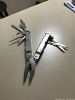 Multi-tool unfolded showing needle-nose pliers, saw blade, knife blade, and other fold-out tools.