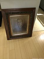 Full view of Victorian portrait painting with wooden frame leaning against wall on wooden floor.