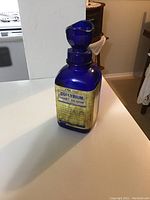 Front view of a cobalt blue glass bottle with a yellowed label showing the Collyrium eye lotion details and a unique eye wash cap.