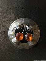 Front view of the circular sterling silver brooch showing intricate Celtic thistle engravings and two large round citrine stones.