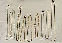 10 assorted gold-like chain necklaces laid flat on a white background, showing various chain link styles and thicknesses.