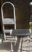 Photo showing a white 2-step foldable ladder and black padded step-up bench placed side by side against a wooden background.