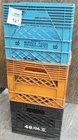 Stack of three milk crates in blue, orange, and black, showing front brand and markings.