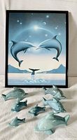 Framed dolphin print with seven carved stone dolphins arranged in front; showing overall items in lot.