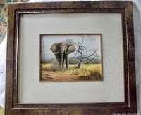 Full view of the framed painting showing elephant and the surrounding landscape with tree and cloudy sky. Frame is a textured dark brown wood and the painting is matted in cream.