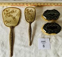 Photo showing the full vanity set including large gold floral hand mirror, matching brush and two smaller silver-coloured brushes with ornate backs and light bristles, all arranged together with a ruler for size reference.