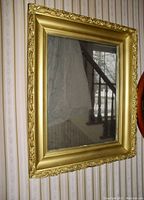Front view of the rectangular mirror showing its ornate gold colored wooden frame with carved edges hanging on wallpapered wall