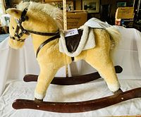 Side angle of large tan plush rocking horse with wooden rocker base and bridle. Shows the white mane, tail and fleece saddle trimming.