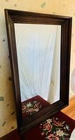 Front angled view of the large pine framed mirror against a wallpapered background showing the frame color and wood grain detail.