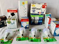 Large assortment of light bulbs with various packaging and types, LED bulbs on green cards in front, boxed incandescent and compact fluorescent bulbs in the back.