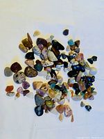 Photo showing a scattered collection of various tumbled, polished stones of different colors, sizes, and patterns on a white background.
