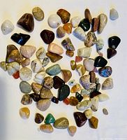 Top-down photo of about 60 mixed tumbled polished gemstones in assorted colors and sizes on a white background.