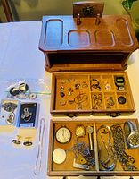 Overview of the full wooden jewelry box with multiple compartments containing watches, rings, necklaces, pins, and cufflinks.