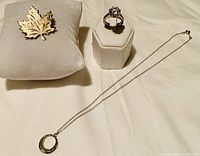 Photo showing sterling silver necklace with circular pendant, ring with large stone on display stand, and Canada Maple Leaf brooch on cushion.