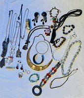 Photo showing entire collection of vintage jewelry including necklaces, bracelets, rings, earrings, a watch, and brooches spread out on white cloth.