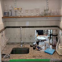 Countertop and shelf with various glassware including decanter, multiple glasses, and several bottle openers and stoppers laid out showing variety