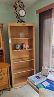 Photo showing the full wooden bookcase with five shelves in a room setting, light wood finish, used condition with scratches.