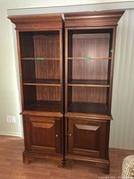Front view of two matching wooden bookcases side by side showing upper open shelves and lower cabinet doors closed.