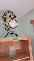 Photo of clock on metal flower and bird statuette showing colorful flowers and Roman numeral clock face.