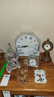 Image showing five clocks including a large octagonal wall clock, three smaller mantel clocks, and two decorative switch plate covers on a table.