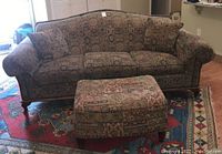 Full view of the patterned three cushion sofa with two matching pillows and ottoman in front