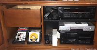 Photo showing Sony receiver, Sony CD/DVD player, Pioneer CD player and cassette deck, remote controls, and media discs inside wooden cabinet.