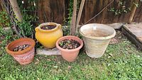 Photo showing all four flower pots of varying shapes and sizes on grass outdoors, with some soil and leaves inside.