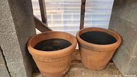 Two medium-sized terracotta flower pots with leaf imprints on the exterior, showing some wear and dirt inside.