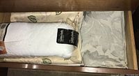 Folded white and beige floral embossed linens in a drawer