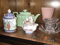 Wide shot showing all items on shelf including teapots, green covered dish, glassware, miniature tea set, crystal bowl with dish and small metal figures.