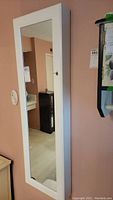Front side view of white jewelry cabinet showing full-length mirror mounted on wall.