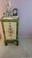 Full front view of the jewelry cabinet showing green frame, floral painted drawers, and mirror on top.