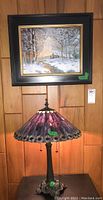 Photo showing the lamp and framed winter landscape painting hung on wall behind it.