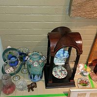 Photo of wooden and glass display stand with miniature tea sets and various decorative glassware and figurines.
