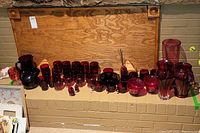 Full display of red glassware items arranged on a brick ledge including cups, plates, pitchers, footed glasses, and vases.