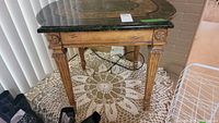 Front and side angle view of a wooden side table with stone-look top and carved details on legs and apron.