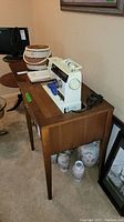 Singer sewing machine with basket and accessories on a wood cabinet with ceramic items underneath.