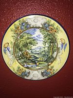 Colorful decorative plate with cherubs, flowers, and a central nature landscape scene