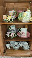 Full view of three shelves showing tea set cups with saucers and floral themed oil lamps